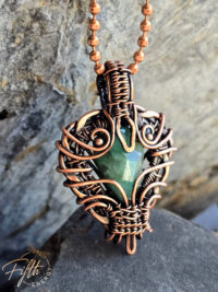 Close-up of a handmade emerald pendant wrapped in American-made copper, crafted by a U.S. artisan. The shimmering green gemstone and warm copper tones create a bold, rustic, one-of-a-kind necklace.