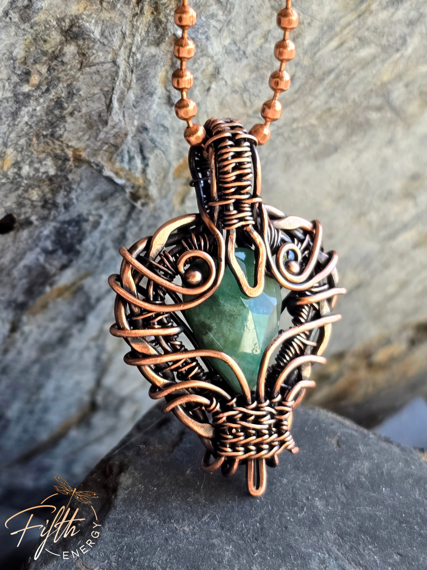 Close-up of a handmade emerald pendant wrapped in American-made copper, crafted by a U.S. artisan. The shimmering green gemstone and warm copper tones create a bold, rustic, one-of-a-kind necklace.