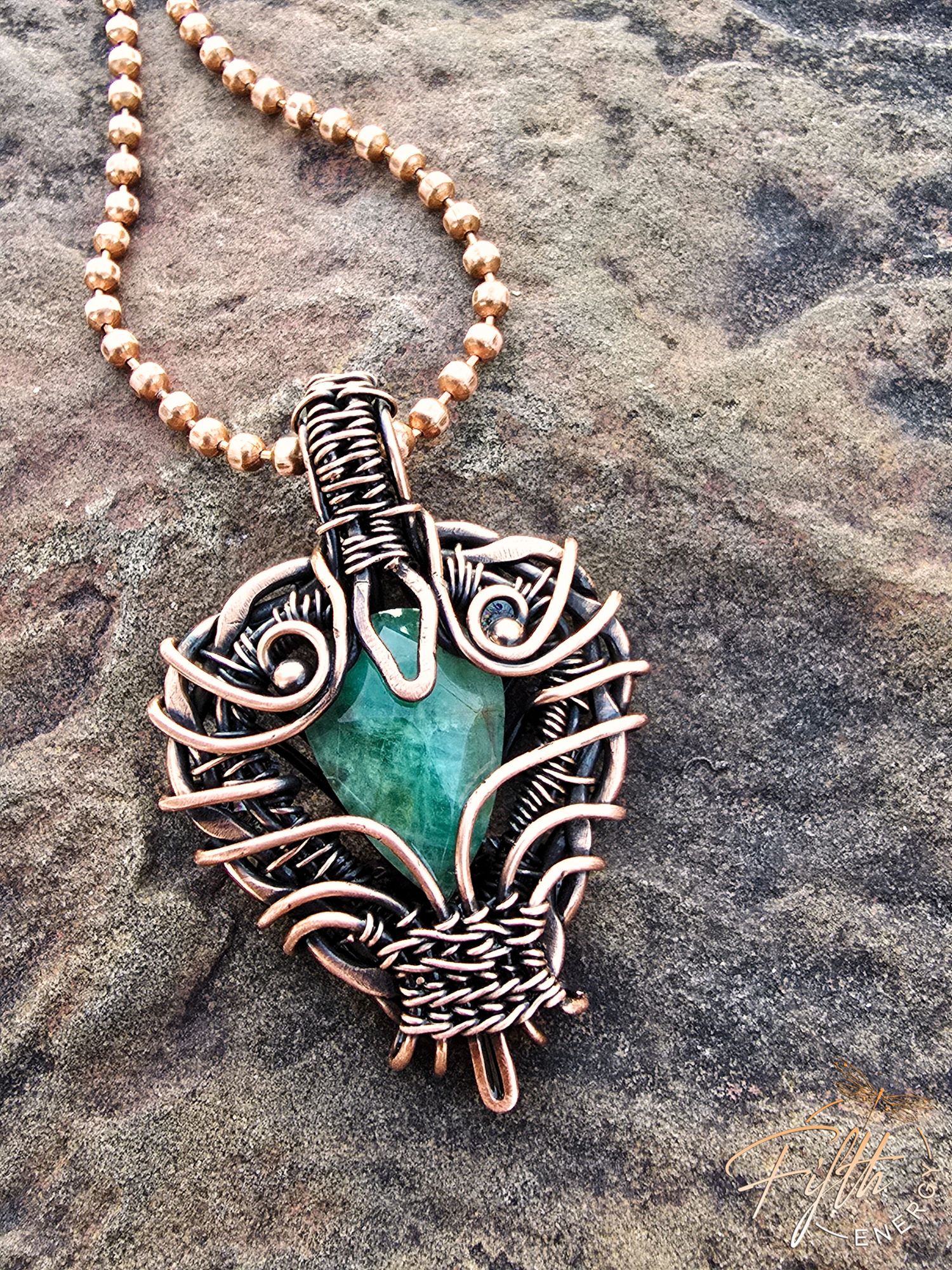 Copper Encased Emerald Necklace 4 Close-up of a handmade emerald pendant wrapped in American-made copper, crafted by a U.S. artisan. The shimmering green gemstone and warm copper tones create a bold, rustic, one-of-a-kind necklace.